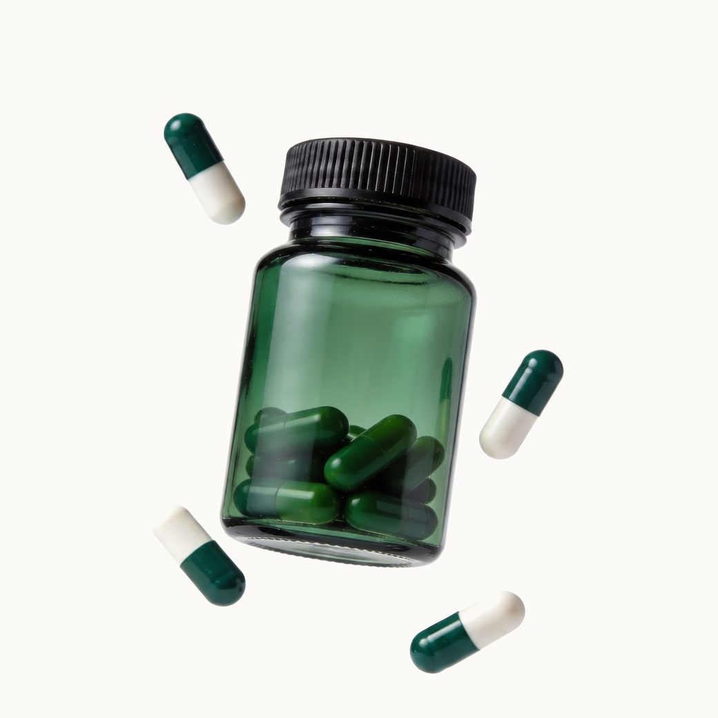 Green glass supplement bottle floating with capsules